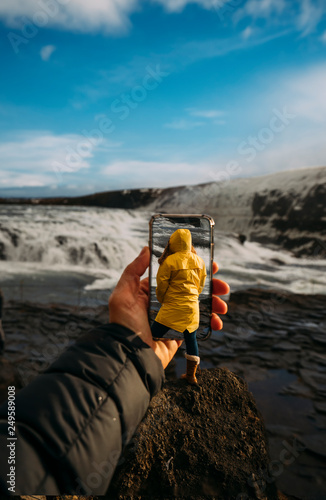 D montage of man taking smartphone picture of Iceland's landscape and woman wearing yellow raincoat photo