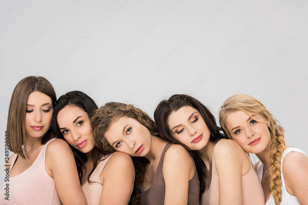 attractive young women putting heads on shoulders of each other isolated on grey