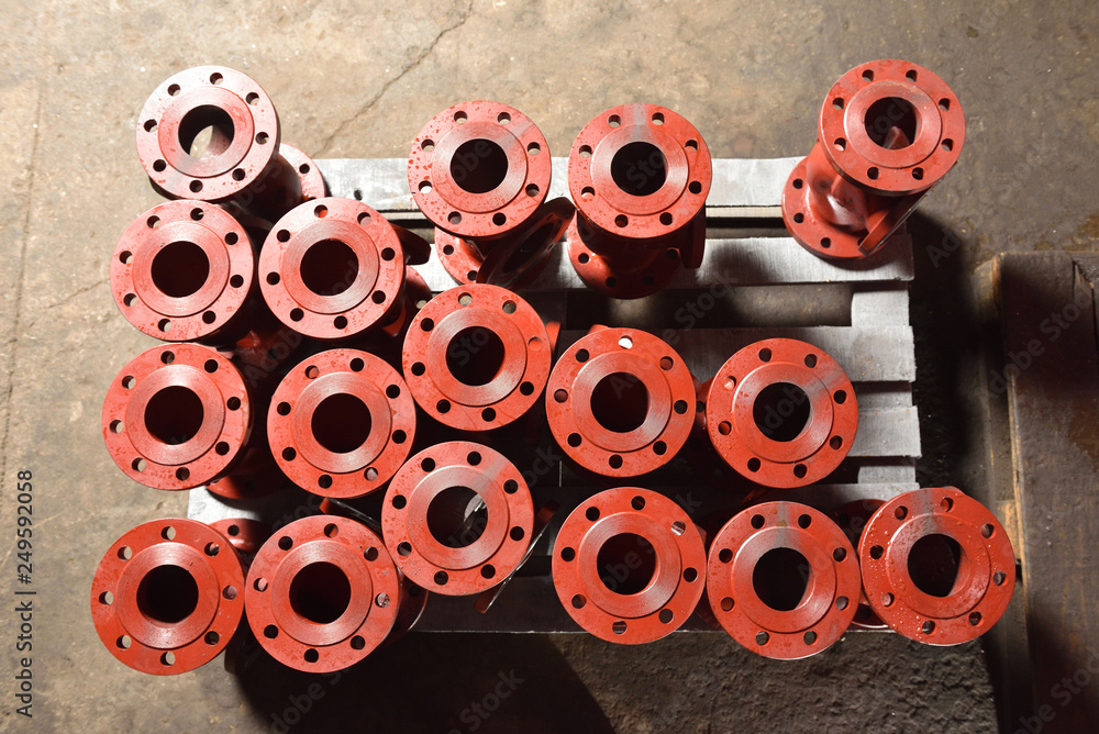 Fototapeta premium Iron or cast iron pipes, bases for creating valves, lie on a wooden panel before further processing on a milling machine. Red bases to create valves in the factory