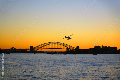 Sunset view of a seaplane flying in the orange sky by the iconic steel Sydney Harbour Bridge in New South Wales, Australia © eqroy