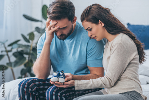 selective focus of grieving parents sitting on bed and holding baby shoes at home photo