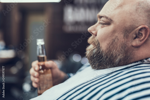 Charming man sitting in barber shop with beer