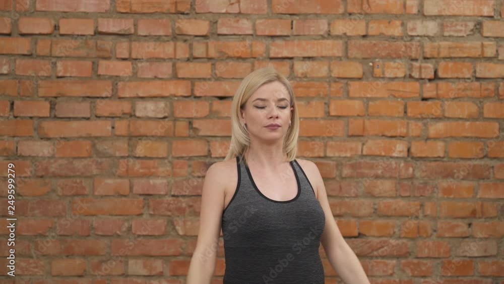 A pretty pregnant blonde in dark tank top standing with her eyes closed, raising smoothly her hands up and down through the sides. A pregnant woman exercising against a brick wall in the background A pretty pregnant blonde in dark tank top standing with her eyes closed, raising smoothly her hands up and down through the sides. A pregnant woman exercising against a brick wall in the background