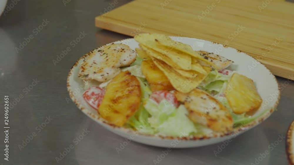 Plate with delicious Cesar salad is on table, cook is adding chips on top Plate with delicious Cesar salad is on table, cook is adding chips on top