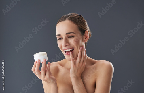 Lovely young woman looking on face cream and opening wide mouth