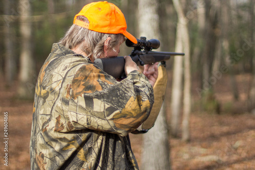 Man shooting gun in the woods with blaze orange hat