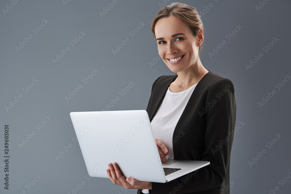 Charming lady looking at camera and holding laptop in hands Charming lady looking at camera and holding laptop in hands