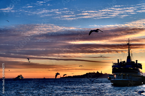 Beautiful suset in Bosphorus Channel with ferryboat, Istanbul, Turkey. Ship at Besiktas. Seaguls fly in Istanbul at suset.