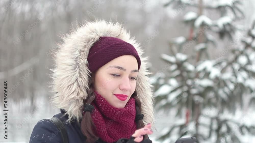 Beautiful young girl is actively flipping through the news feed on her smartphone while walking in a winter park. Portrait. Beautiful young girl is actively flipping through the news feed on her smartphone while walking in a winter park. Portrait.
