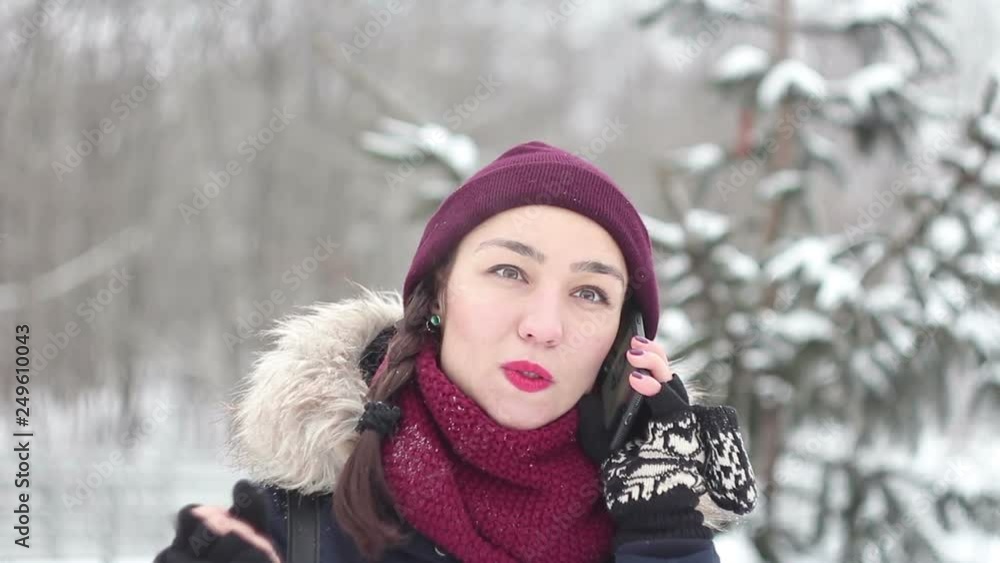 Beautiful young girl talking on her smartphone while walking in a winter park. Portrait. Beautiful young girl talking on her smartphone while walking in a winter park. Portrait.