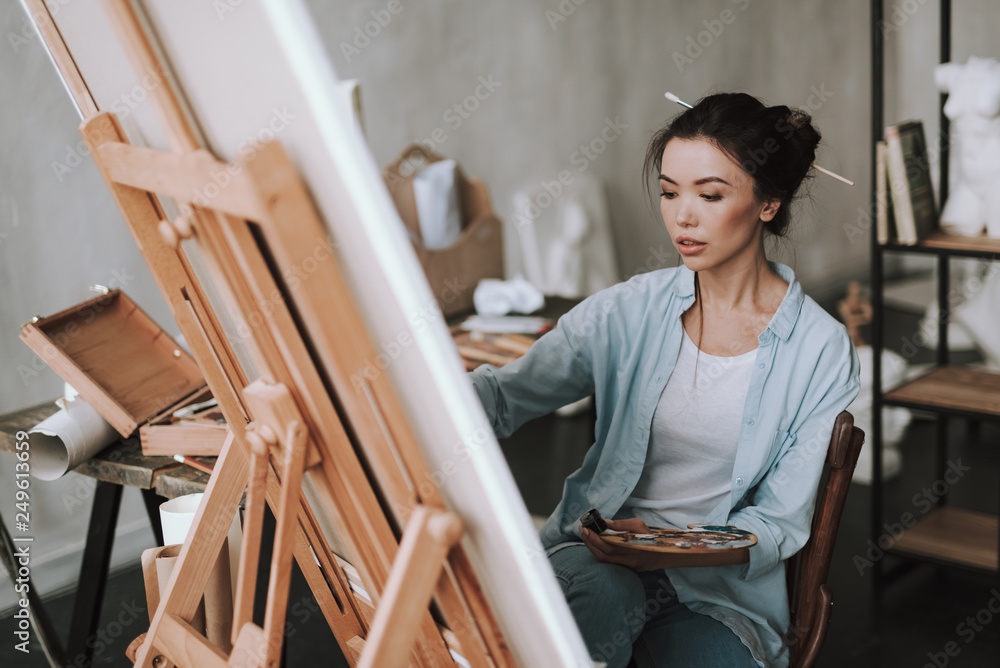 Waist up of calm lady using artist palette while drawing Waist up of calm lady using artist palette while drawing