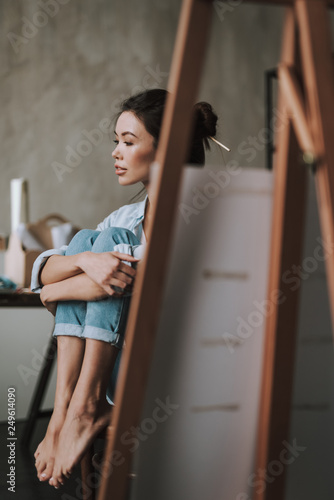 Peaceful artist hugging her legs while sitting on the chair