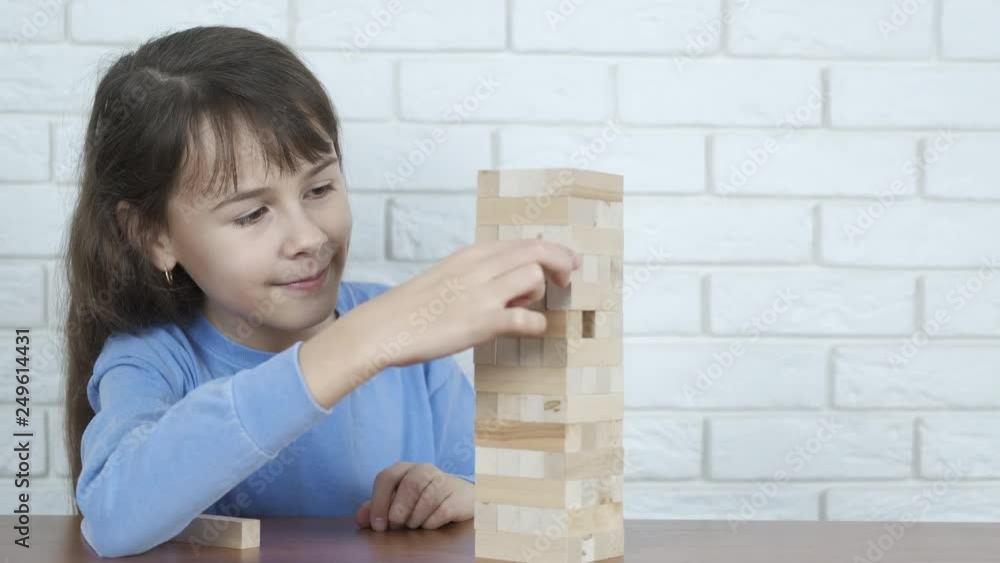 A child is playing with wooden blocks. A little girl plays Jenga. Child and educational board game. A child is playing with wooden blocks. A little girl plays Jenga. Child and educational board game.