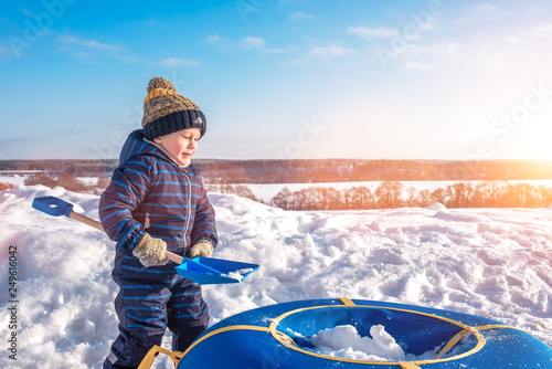 Little boy with a snow shovel in winter in the park. Happy sleeps snow in tubing, in casual wear. photo