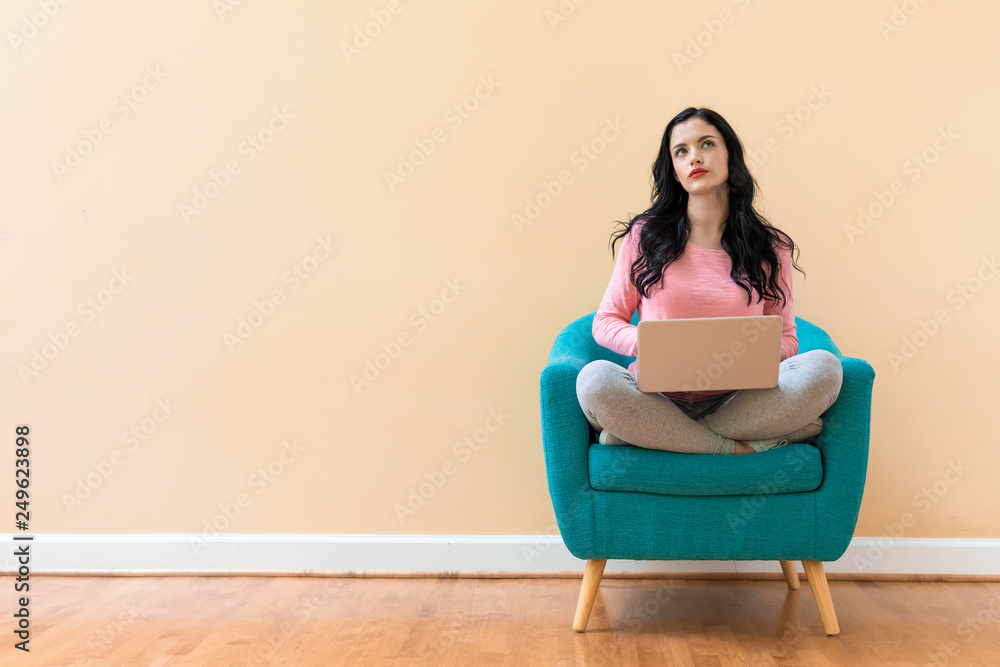 Young woman using her laptop on a blue chair Young woman using her laptop on a blue chair