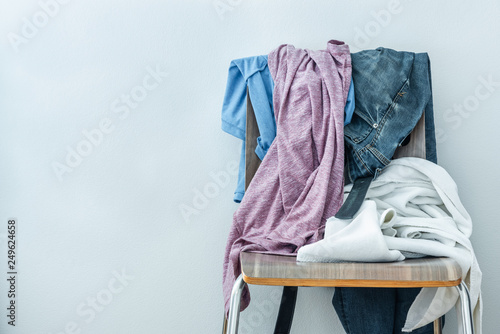 heap of clothes and white towel stacking and hanging on wooden chair on white wall background