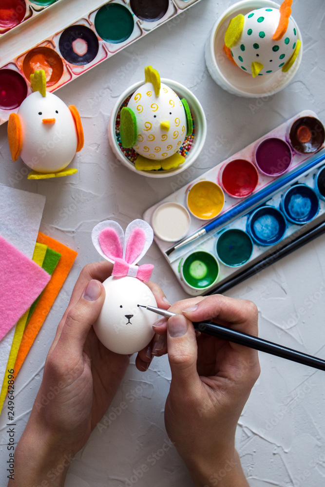 Preparation for Easter. Multi-colored paint, hands in the frame paint the eggs. handmade chickens and Bunny from the egg