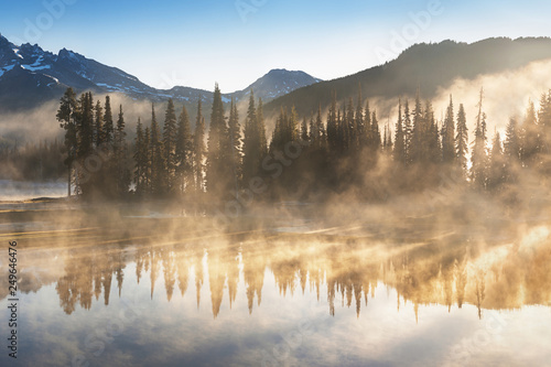 South Sister i Broken Top odbijają się nad spokojnymi wodami jeziora Sparks o wschodzie słońca w Cascades Range w środkowym Oregonie, USA, w świetle wczesnego poranka. Poranna mgła unosi się z jeziora w drzewa.