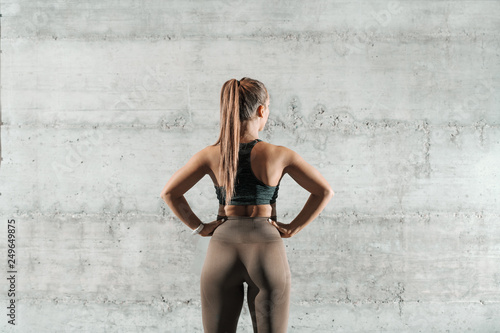 Принти на полотні Caucasian sporty woman dressed in sportswear and with ponytail holding hands on hips and standing in the gym
