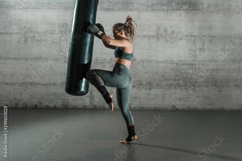 Caucasian woman in sportswear and with boxing gloves kicking bag in the gym. Full length. Wall in background. © dusanpetkovic1