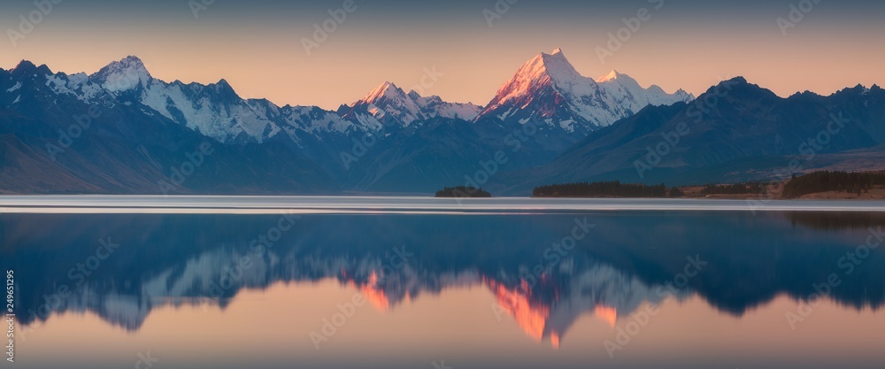 Snowy mountain range reflected in the still water of Lake Pukaki, Mount Cook, South Island, New Zealand. The turquoise water comes from Mt. Cook and Tasman glacier. Popular travel destination 