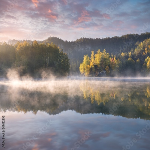 Autumn forest reflected in water. Colorful autumn morning in the mountains. Colourful autumn morning in mountain lake. Foggy autumn sunrise. Beautiful autumn background concept.