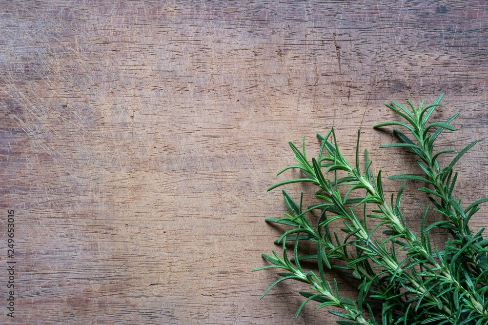 Obraz premium Rosemary plant on wooden rustic table from above, fresh organic herbs with copy space for text
