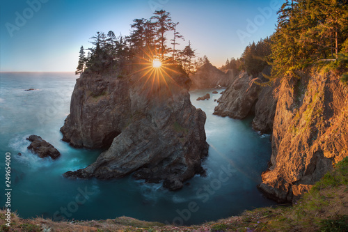 Sunset at Natural Bridges along Samuel H. Boardman State Scenic Corridor, Oregon during a golden hour - sunbeams through trees with dense vegetation. Beautiful seascape with rocks. West Coast USA