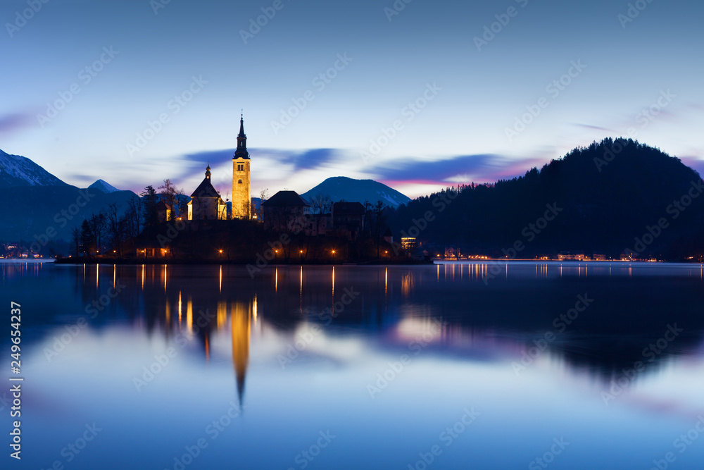 Beautiful view of famous Bled Island (Blejski otok) at scenic Lake Bled with Bled Castle (Blejski grad) and Julian Alps in the background in golden morning light at sunrise in summer, Slovenia