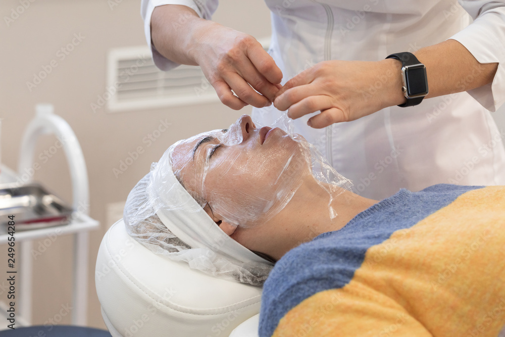 Obraz premium Application of anesthetic cream process to woman before aesthetic laser polishing procedure or injections in the cosmetology medical clinic, beauty salon.