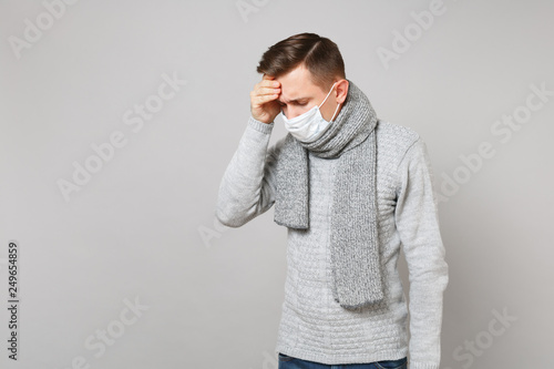 man in gray sweater scarf sterile face mask with lowered head putting hands forehead isolated on grey background. Healthy lifestyle, ill sick disease treatment cold season concept. Mock up copy space.