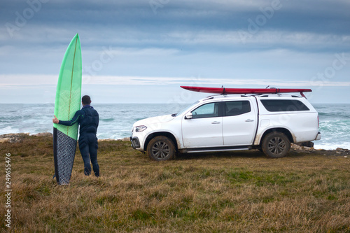 surfista con una tabla de olas gigantes en frente del mar y veh  culo todoterreno con una tabla de surf encima en frente del mar