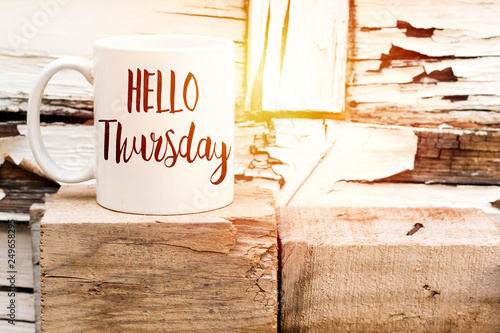 text HELLO thursday on cup of aromatic coffee on wooden cube photo