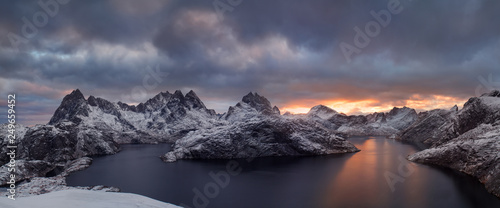 Fototapeta Naklejka Na Ścianę i Meble -  Winter dramatic landscape with snowy mountains, sea, blue and orange cloudy sky reflected in water at sunset. Beautiful Lofoten islands, Norway. Norwegian fjords background. Christmas time concept