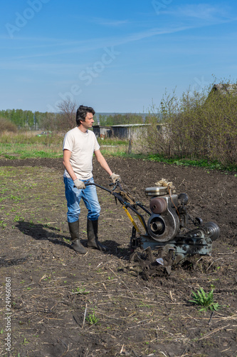 Man with cultivator ploughs ground. Land cultivation, soil tillage. Spring work in the garden. Gardening concept