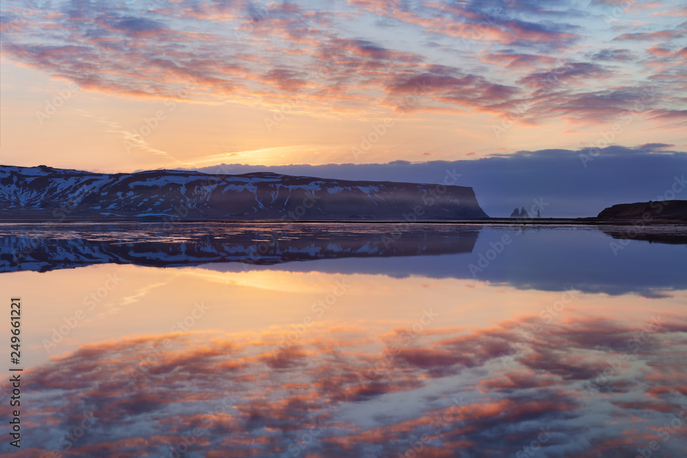 Black sand beach and the mount Reynisfjall, Vik, South Iceland in winter or summer. Panoramic landscape of volcanic mountains and lake in Iceland. Fjord sunset reflection in calm water, dramatic sky