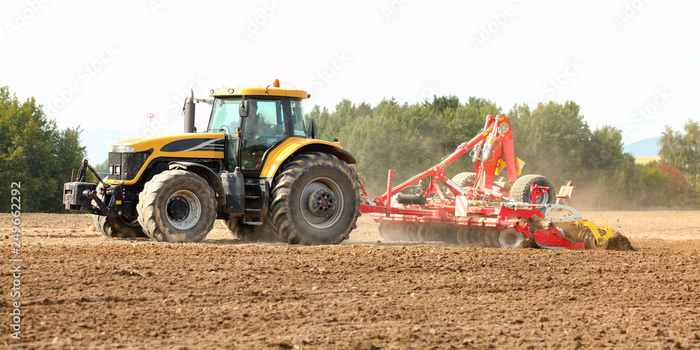 Obraz premium Tractor pulling ploughing / sowing trailer over dry field.