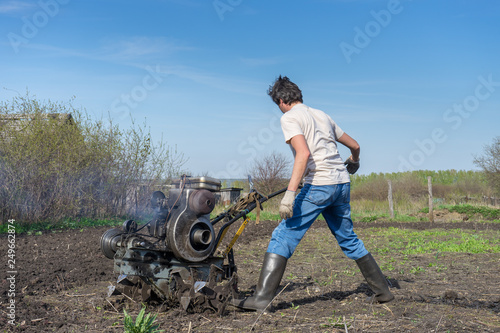 Man with cultivator ploughs ground. Land cultivation, soil tillage. Spring work in the garden. Gardening concept