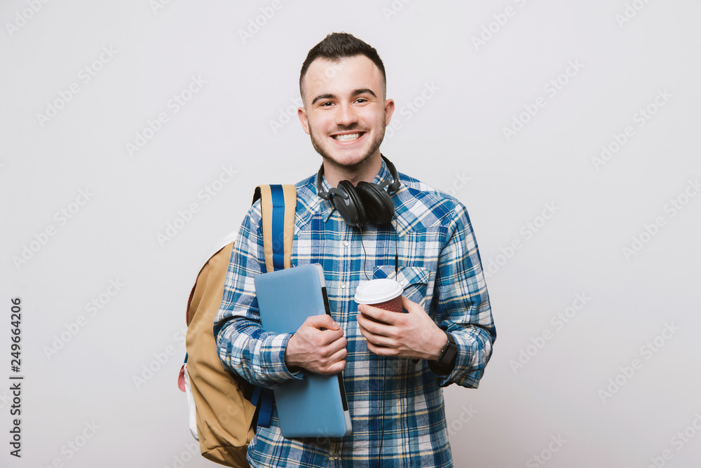 Portrait of young cheerful man with headphones, laptop and coffee. Smiling man going on a travel Portrait of young cheerful man with headphones, laptop and coffee. Smiling man going on a travel