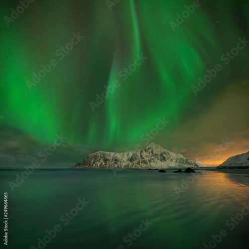 Aurora Borealis on the Lofoten Islands, Norway. Green northern lights above mountains and beach. Night sky with polar sky above arctic circle. Winter landscape with aurora reflection on the water. © Michal