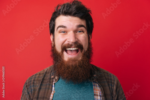 Portrait of an excited bearded man with open mouth isolated over red background