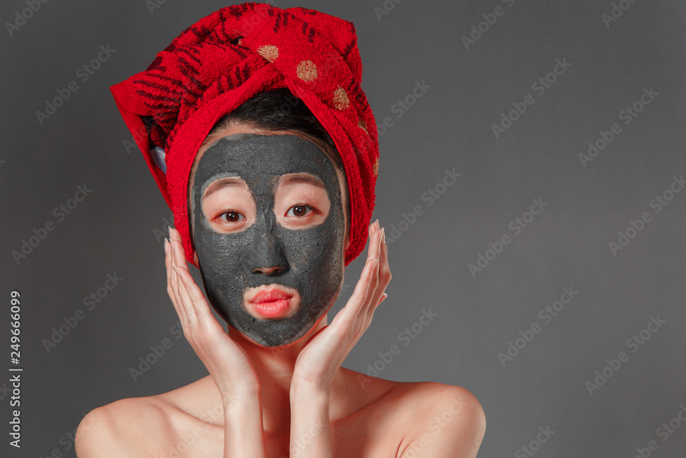 attractive young korean girl with a red towel on her head applied a useful clay mask attractive young korean girl with a red towel on her head applied a useful clay mask
