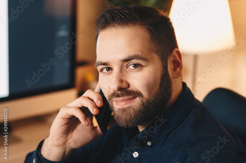 portrait of an aspiring young businessman posing in his home office, looking at the camera while using his cellphone.