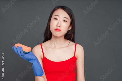 Korean housewife in rubber gloves on her hands holding a sponge, isolat on grey background.