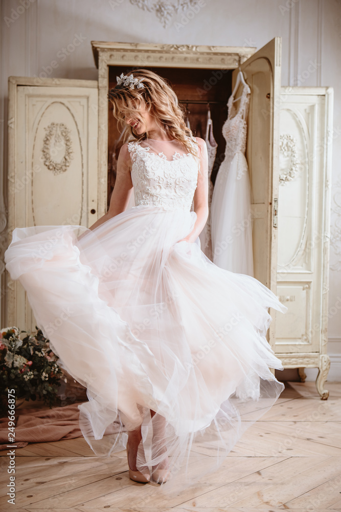 Fototapeta premium Beautiful bride blonde woman sitting near vintage wardrobe full of wedding dresses. fashion beauty portrait 