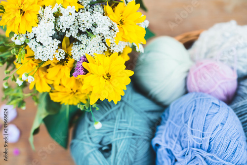 Womens hobby. Skeins of yarn and knitting needles in the basket on wooden background.	Summer flowers