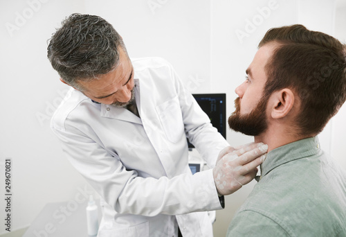 Doctor in medical gloves palpating man's neck.