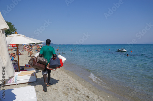 Vendor with counterfeit products on the beach in Chaniotis, Greece. Street vendor selling popular brands replicas bags by a Greek beach shore on a sunny summer day.