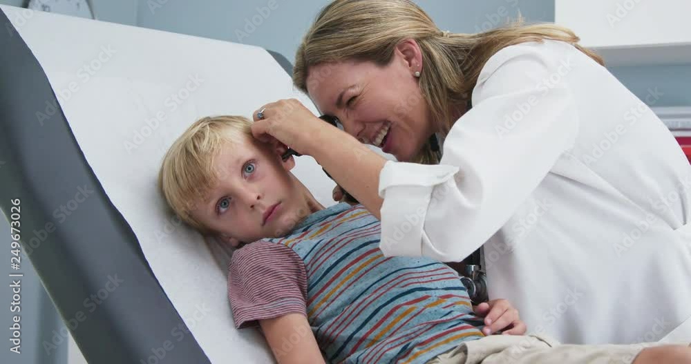Woman doctor giving exam using otoscope to child in pediatrician office. Female pediatrician checking ears of young boy in clinic exam room. Slow motion 4k Woman doctor giving exam using otoscope to child in pediatrician office. Female pediatrician checking ears of young boy in clinic exam room. Slow motion 4k