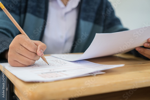 Student taking exams, writing examination on paper answer sheet optical form of standardized test on desk doing final exam in classroom, Education assessment Concept. Soft focus